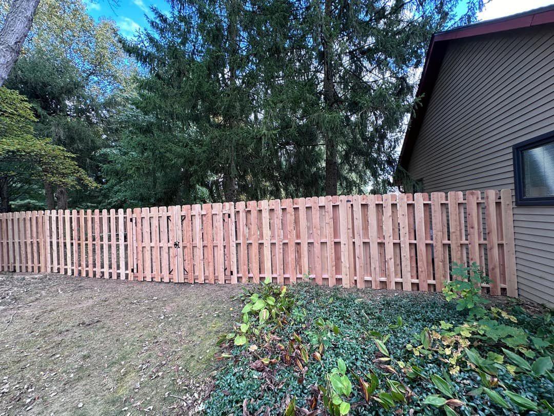 A wooden fence is surrounding a house in a backyard.