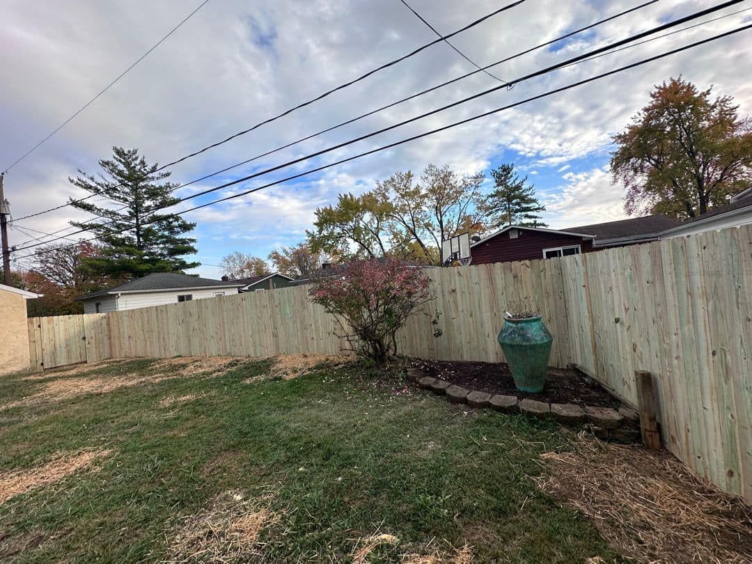 A backyard with a wooden fence and a green vase.