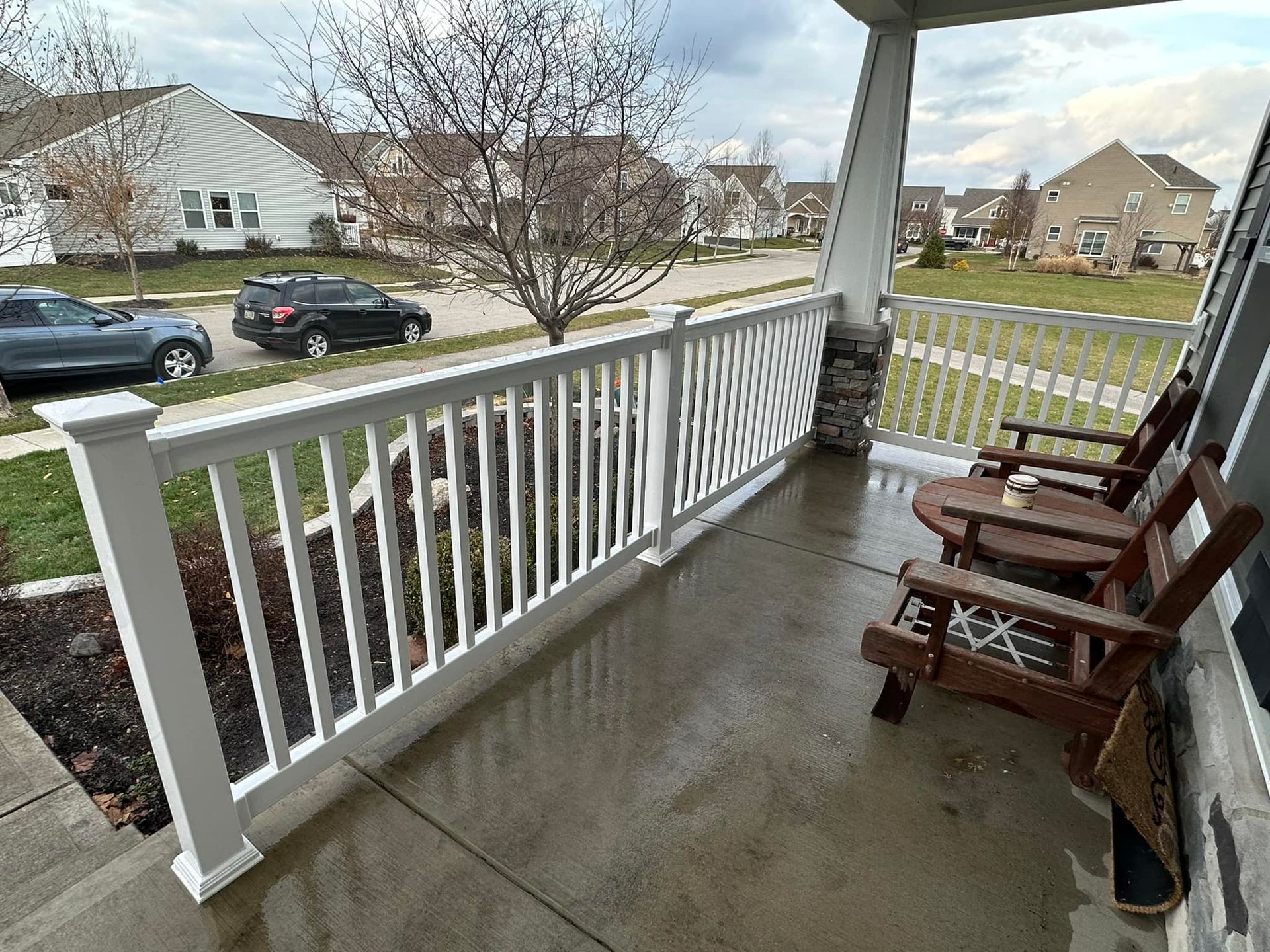 A porch with a white railing and wooden chairs.