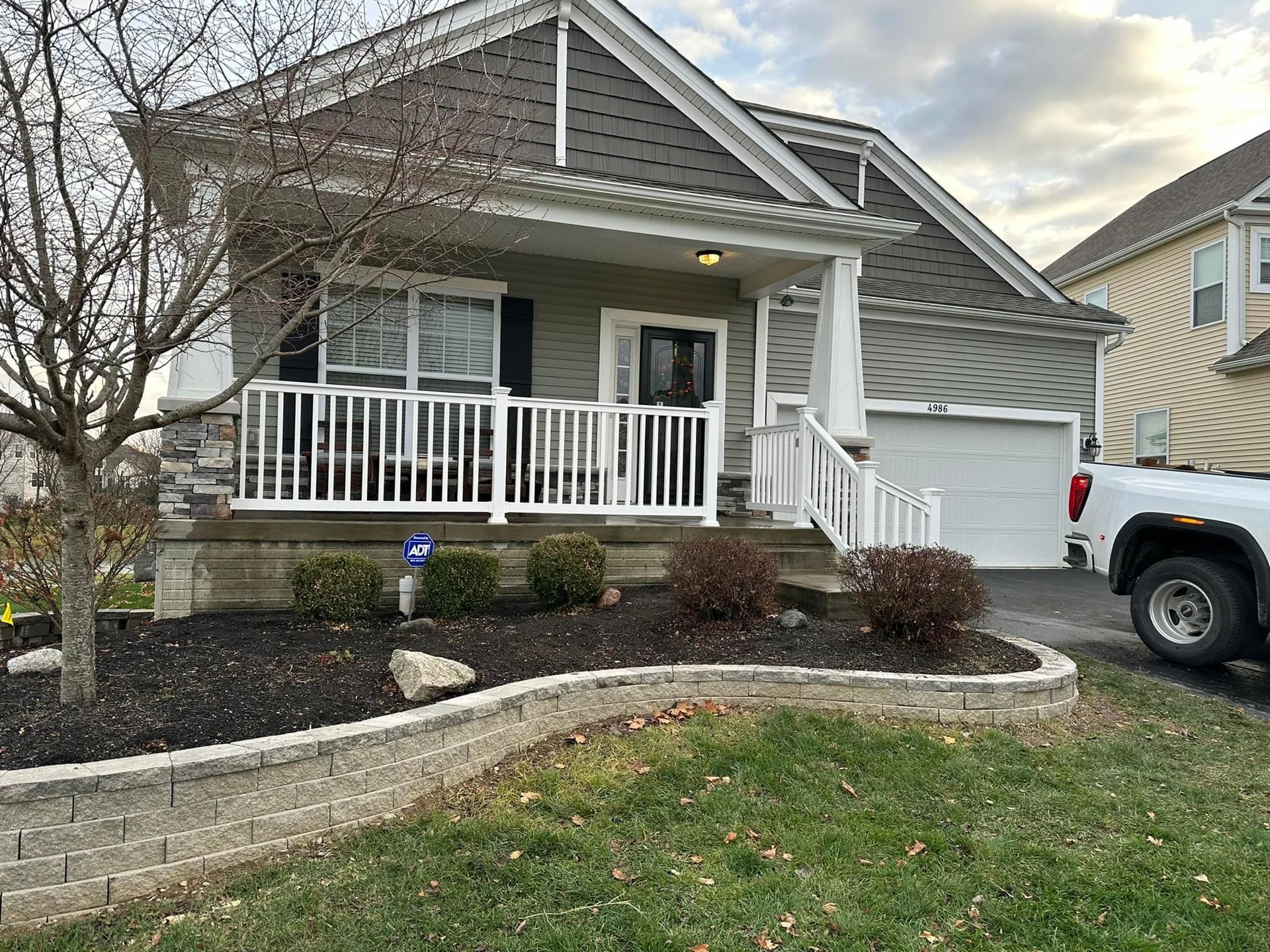 A white truck is parked in front of a house with a porch.
