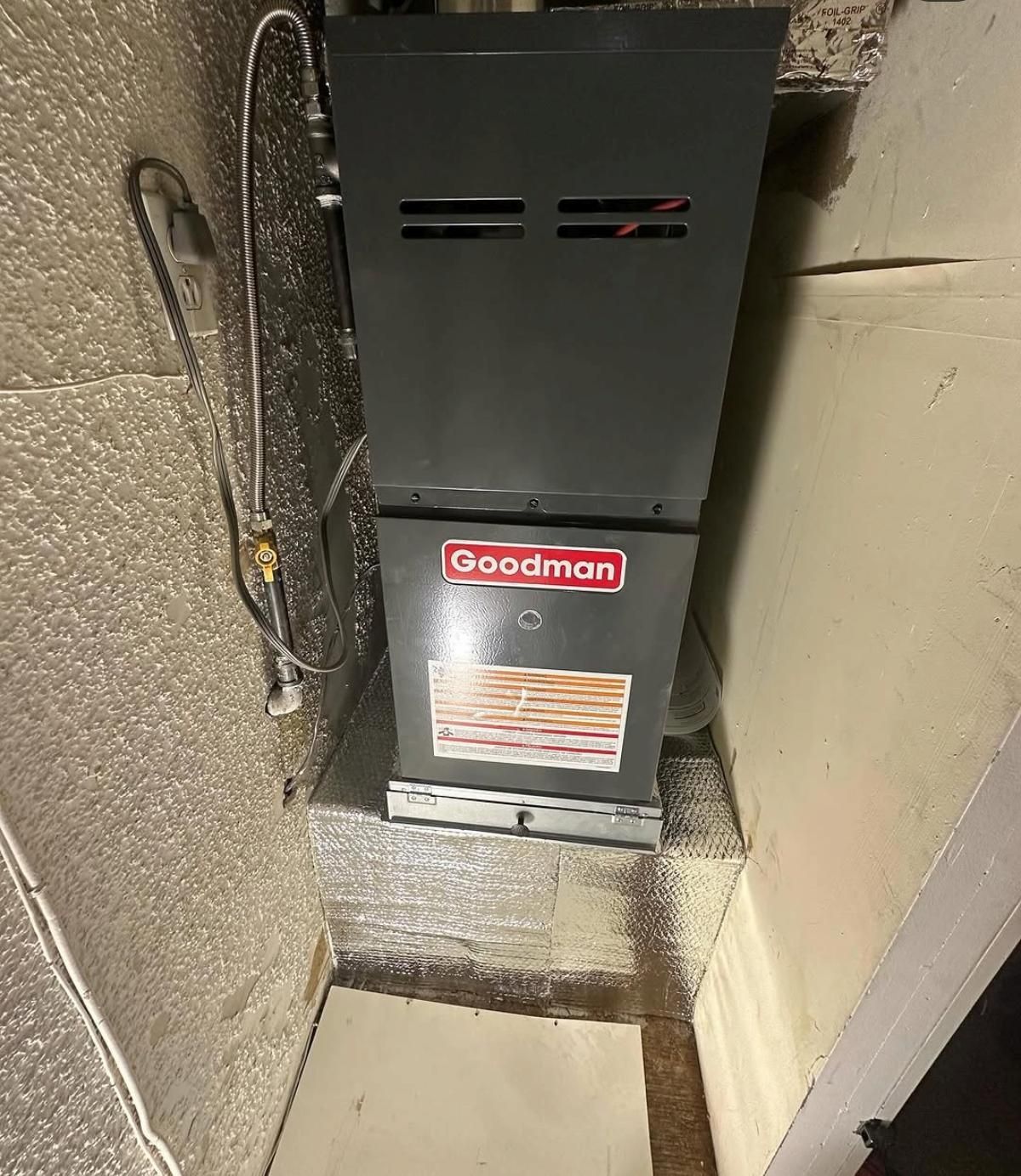 Goodman furnace in a narrow utility closet with exposed insulation and ductwork