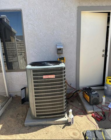 Outdoor air conditioner unit beside a building door, with tools and cables on the ground.