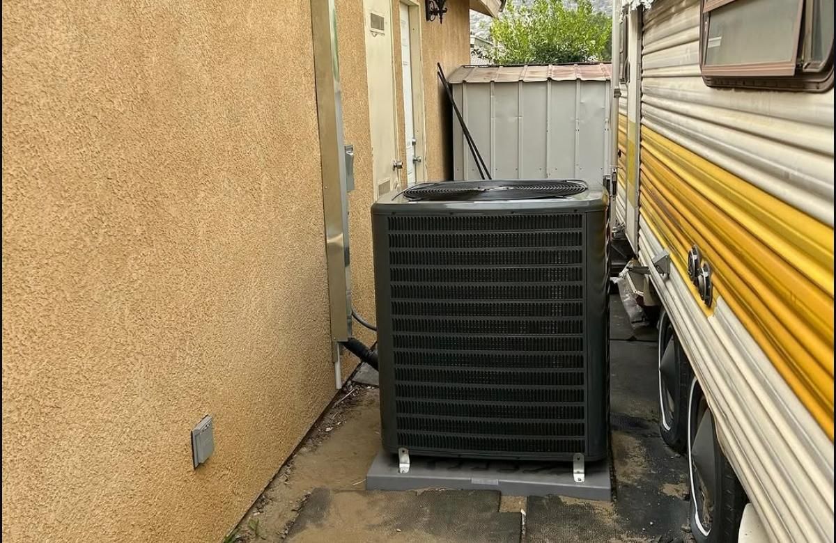 Outdoor AC unit between a tan wall and a yellow RV beside a white fence