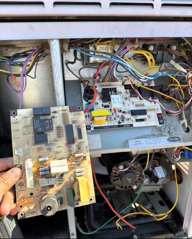 Hand holding a circuit board inside an open appliance with exposed wires and mechanical parts
