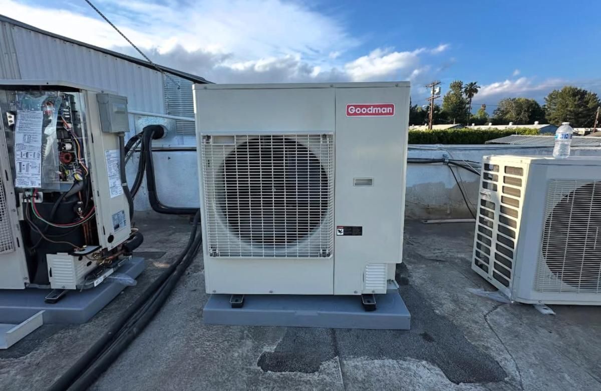 Rooftop HVAC units and ductwork on a flat commercial roof under a blue sky