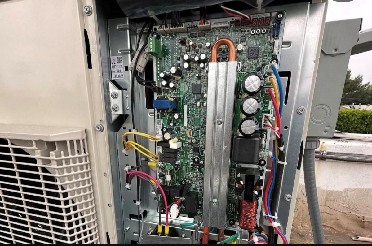 Open electrical control panel with circuit board, wires, and components inside outdoor HVAC unit.