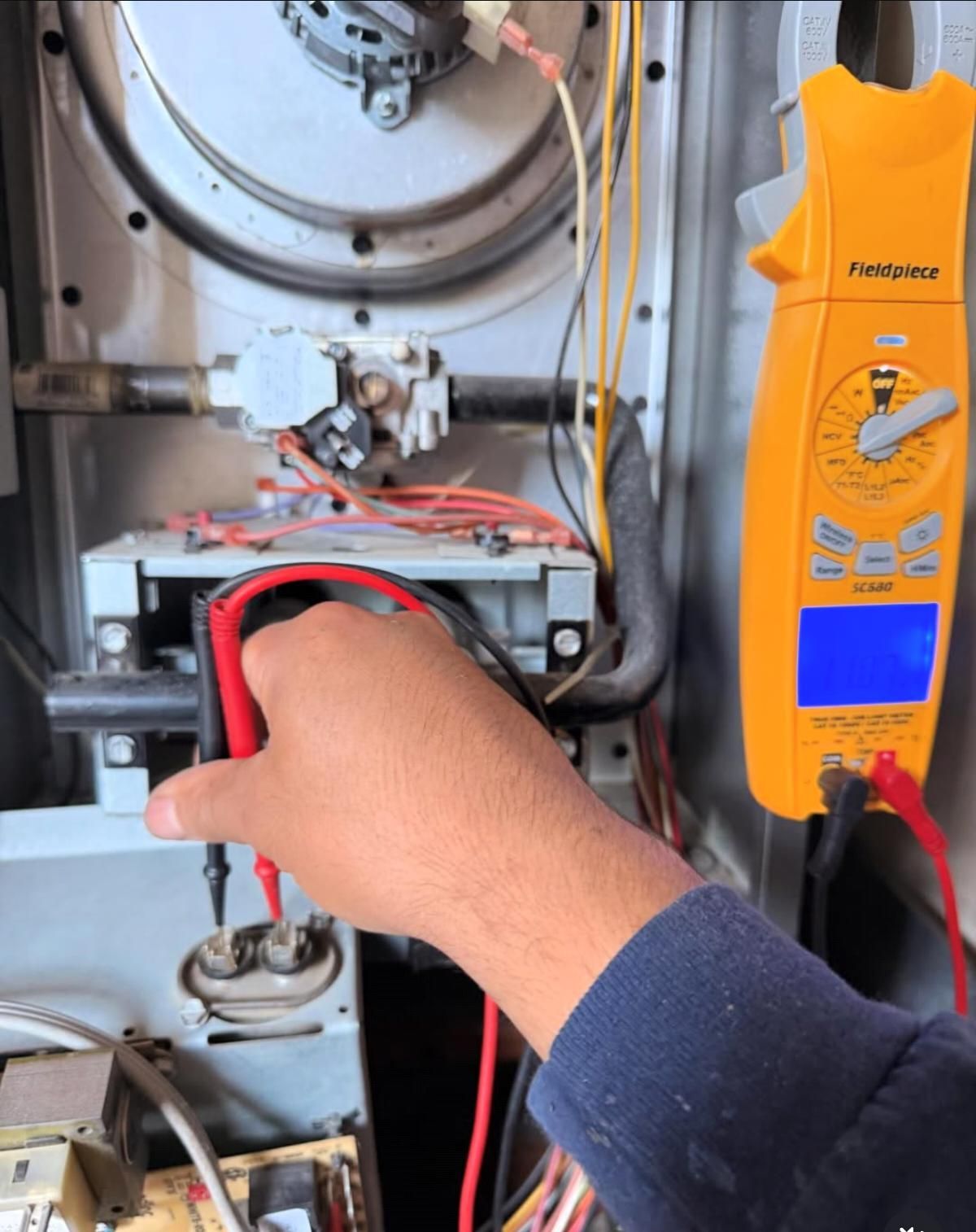 Technician using a multimeter to test wires inside an open furnace panel