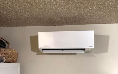 White wall-mounted air conditioner above a gray wall in a room with a textured ceiling