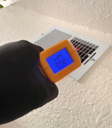 Handheld infrared thermometer aimed at a ceiling vent, showing 51.5 on a blue screen