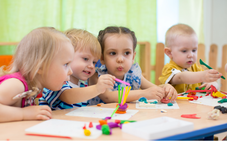 A group of children are sitting at a table playing with play dough. A group of children are sitting at a table playing with play dough.