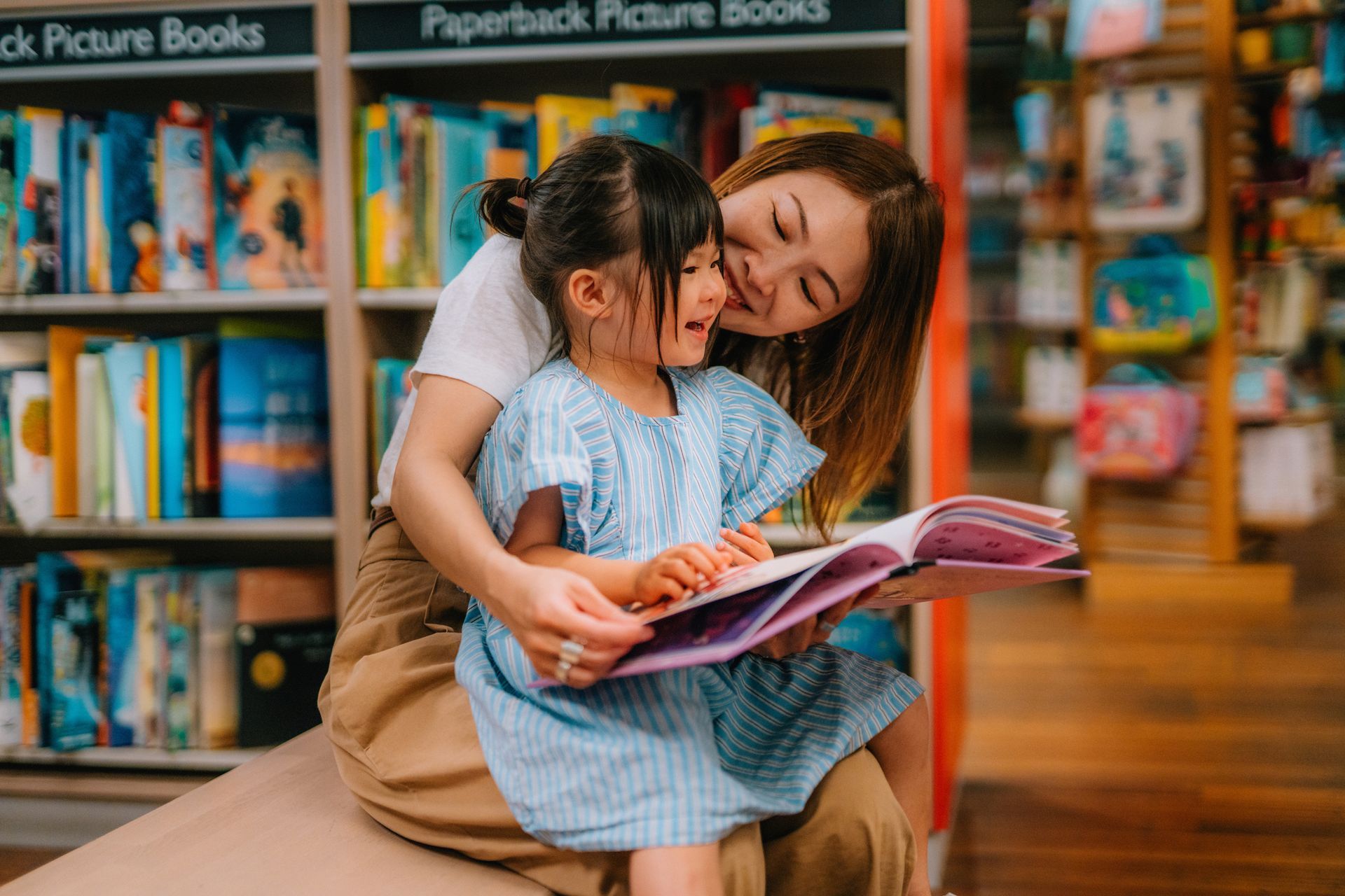 A woman is reading a book to a little girl in a library.