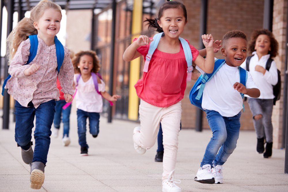 A group of children with backpacks are running down a sidewalk.