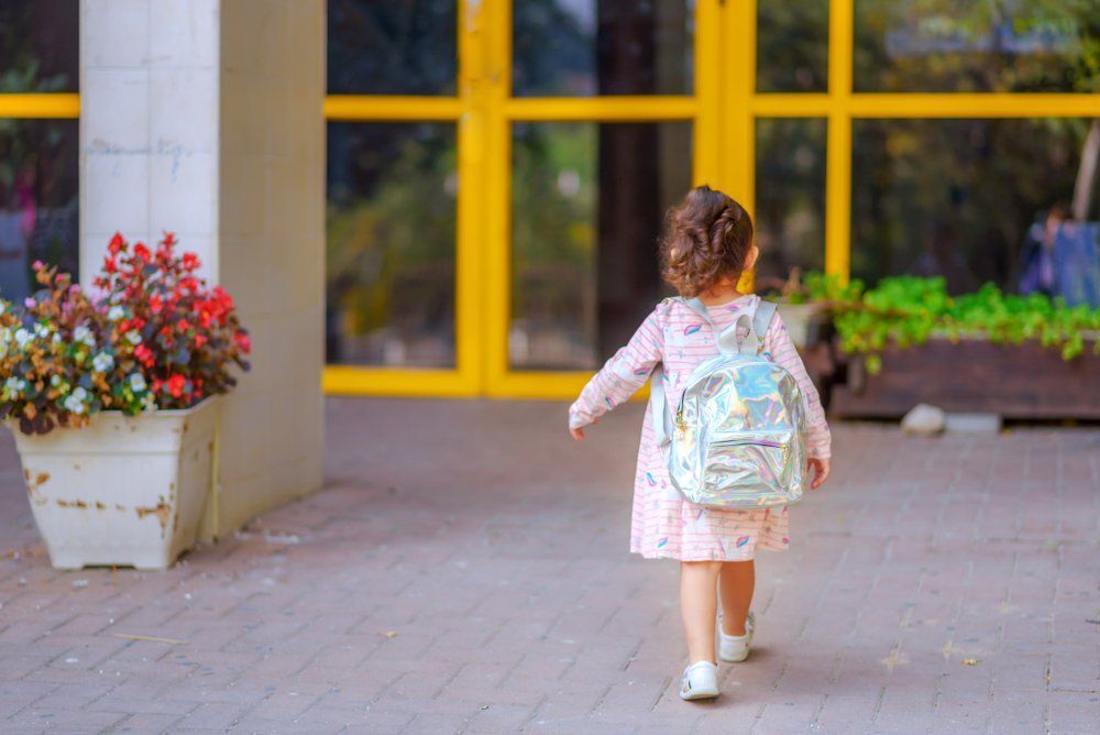 A little girl with a backpack is walking towards a yellow door.