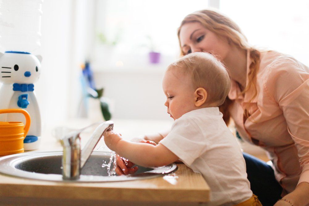 A woman and a baby are washing dishes in a kitchen sink.