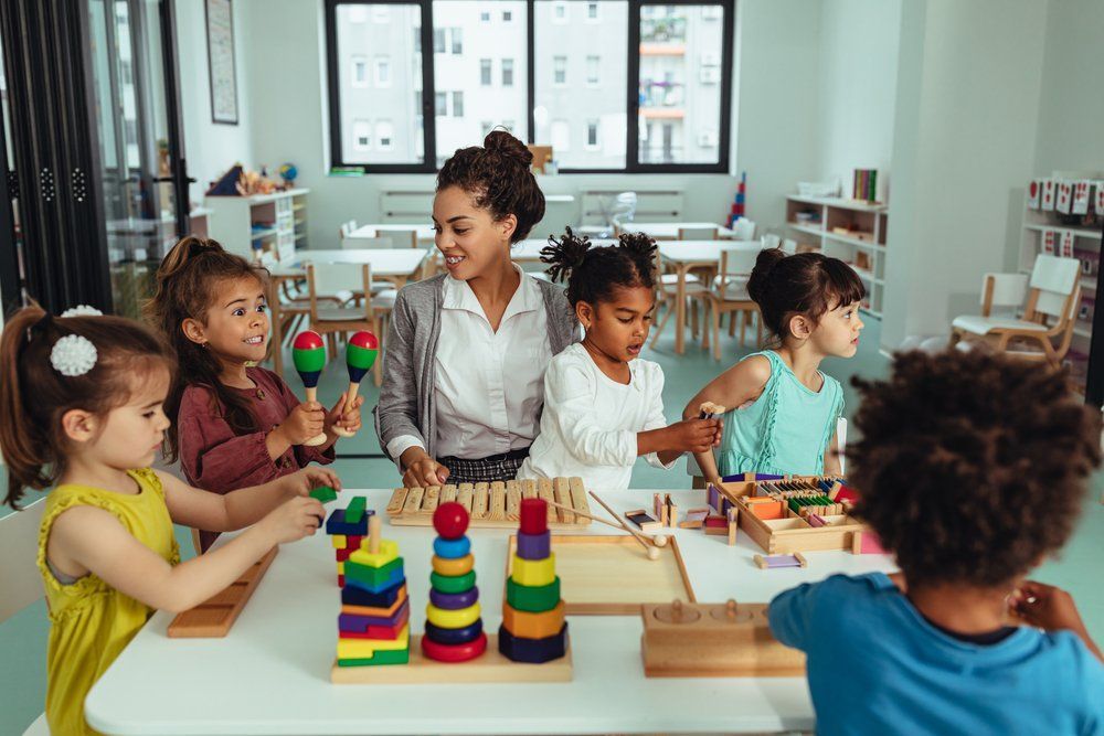 A group of children are playing with toys in a classroom with a teacher.