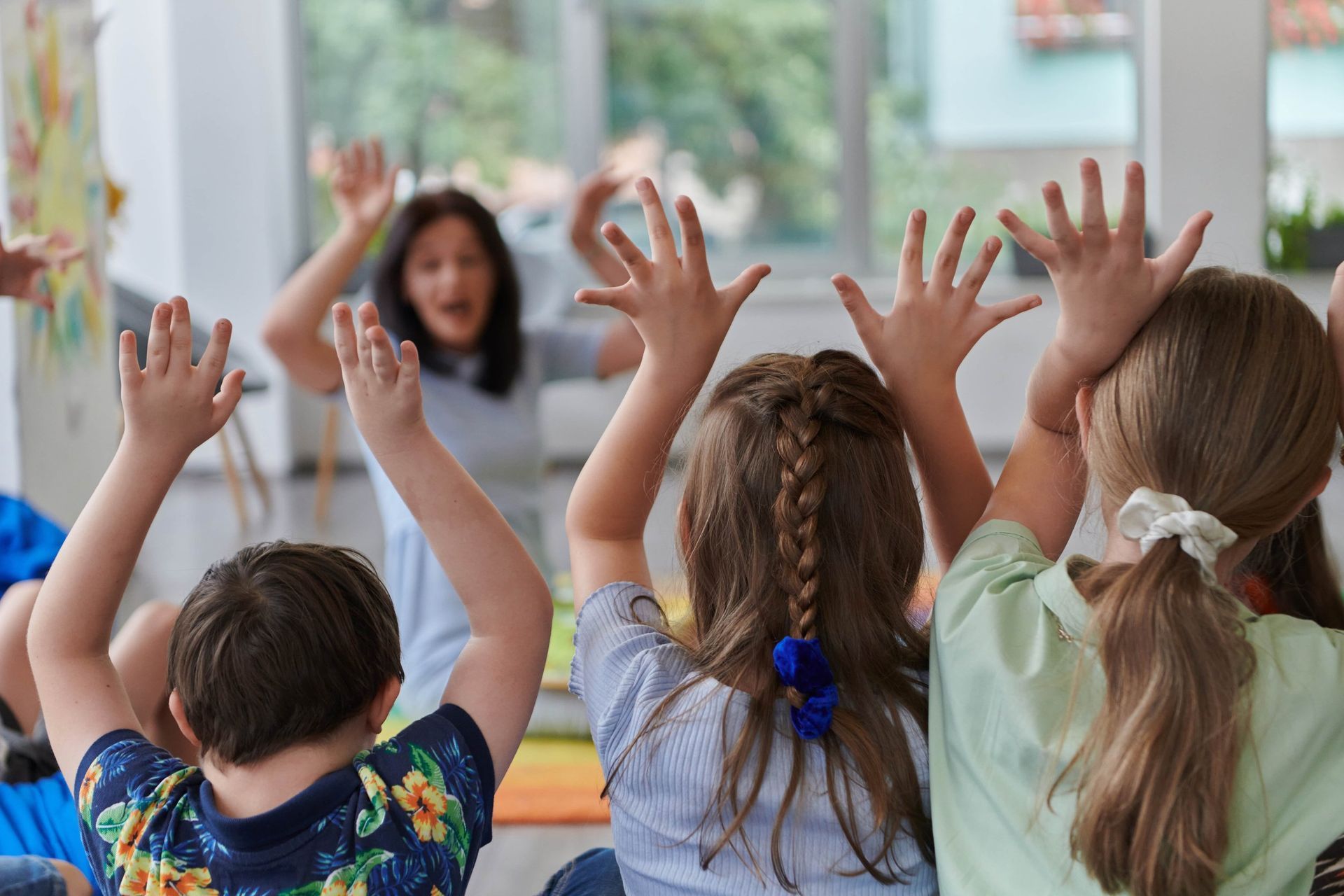 A group of children are sitting on the floor with their hands in the air.