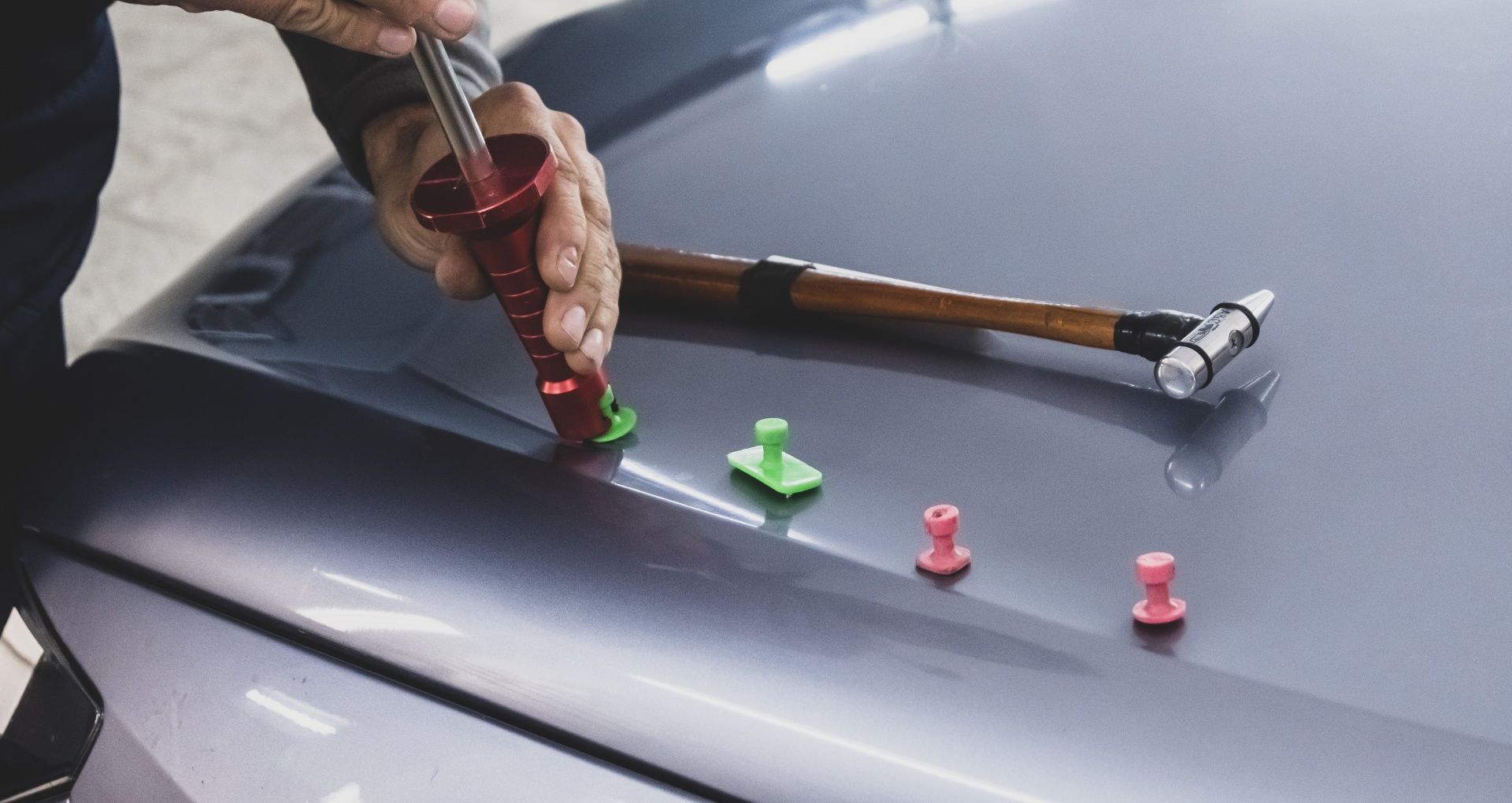 A person is using a hammer to fix a dent on the hood of a car.