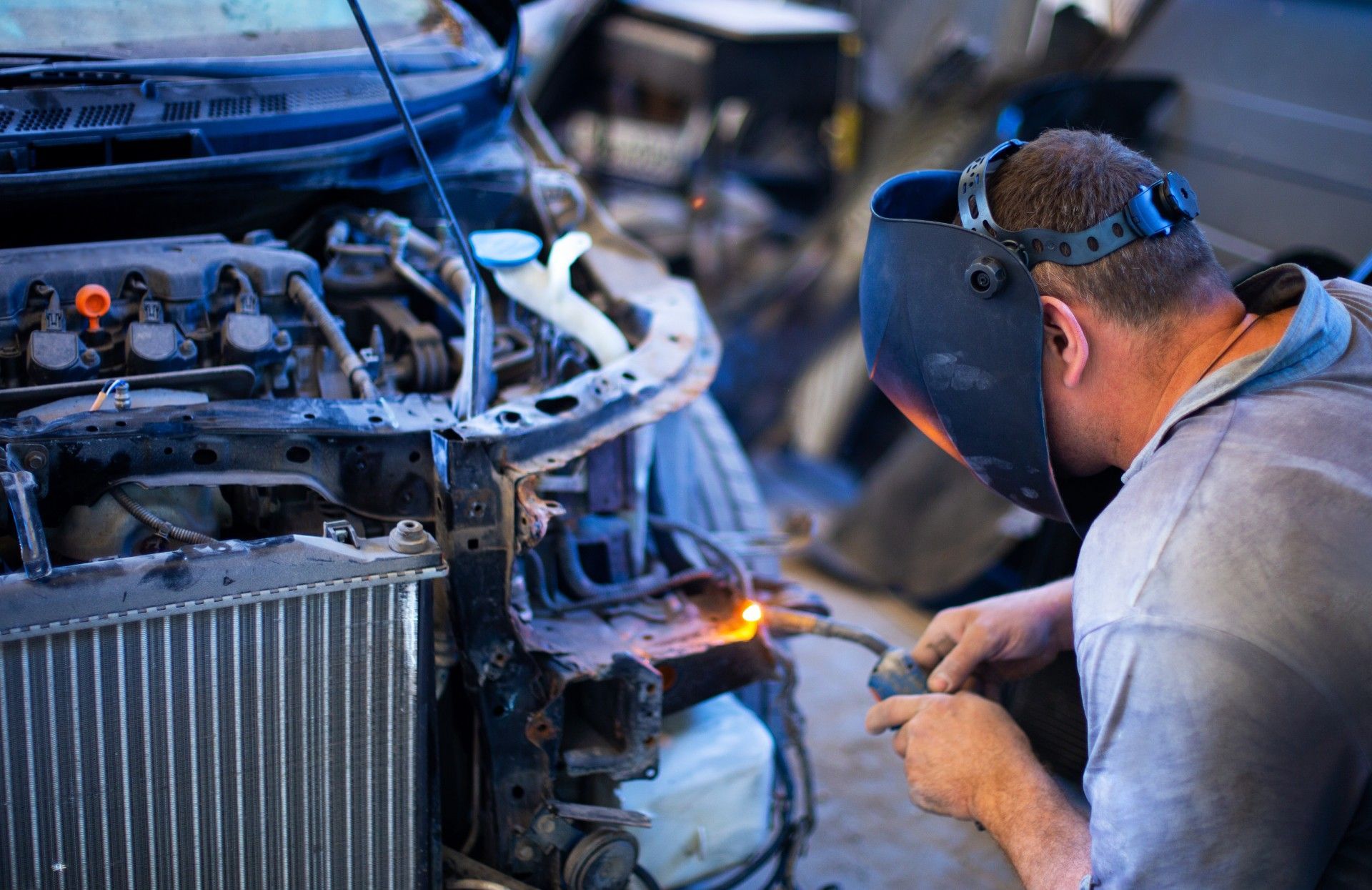 A man wearing a welding mask is working on a car.