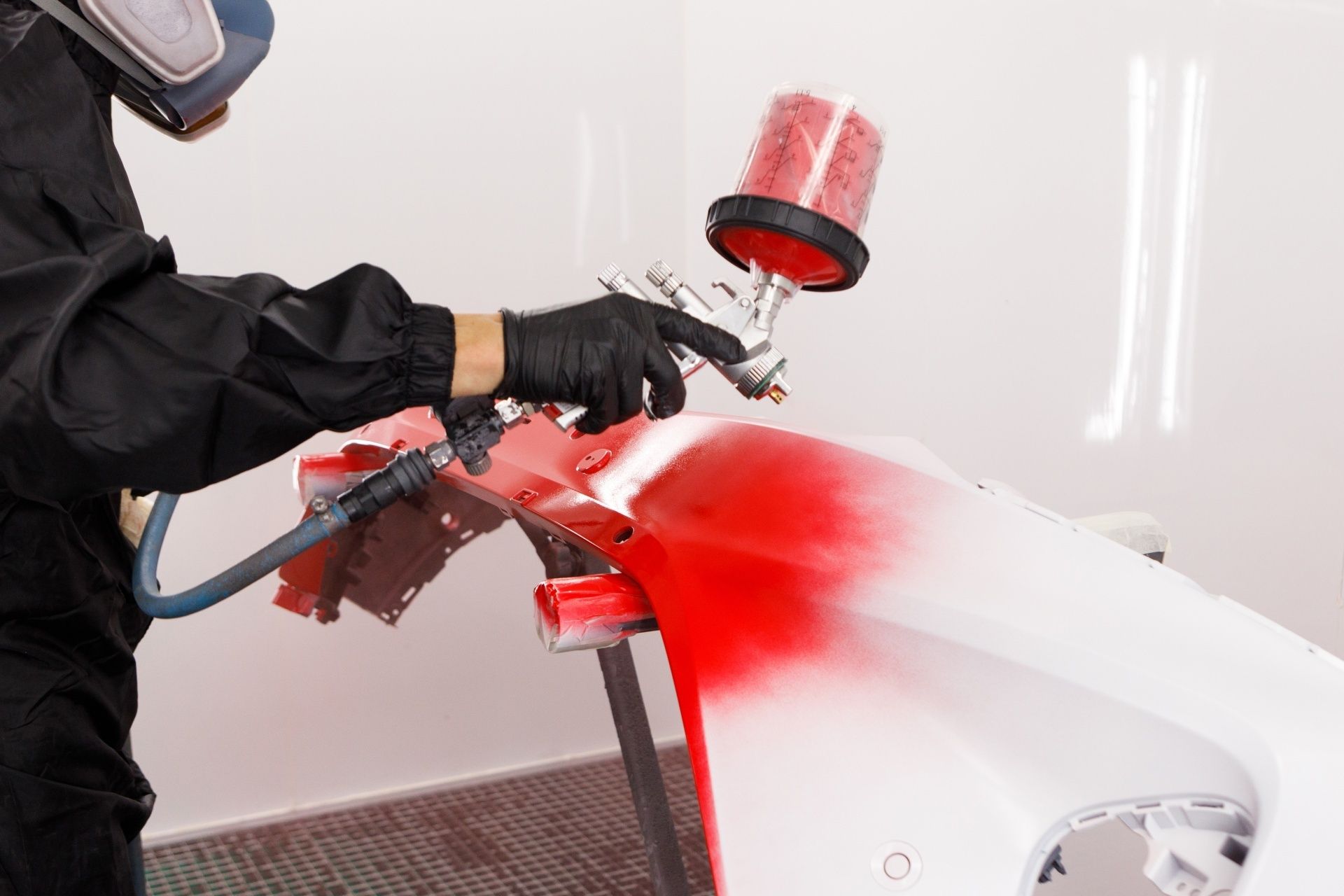 A man painting a car body parts with red paint