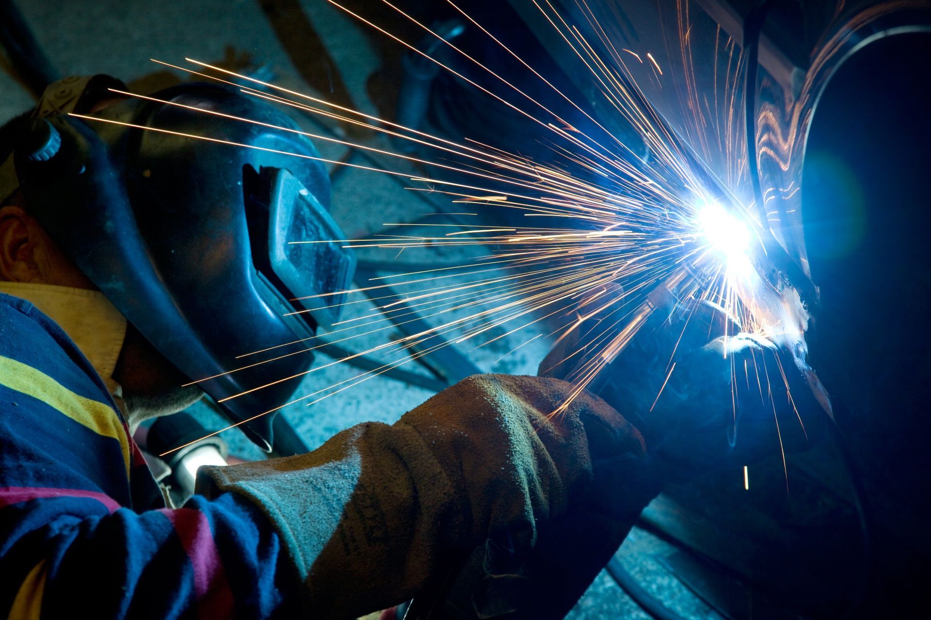 A man wearing a welding mask is welding a piece of metal