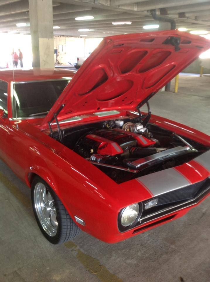 A red car with the hood up in a parking garage