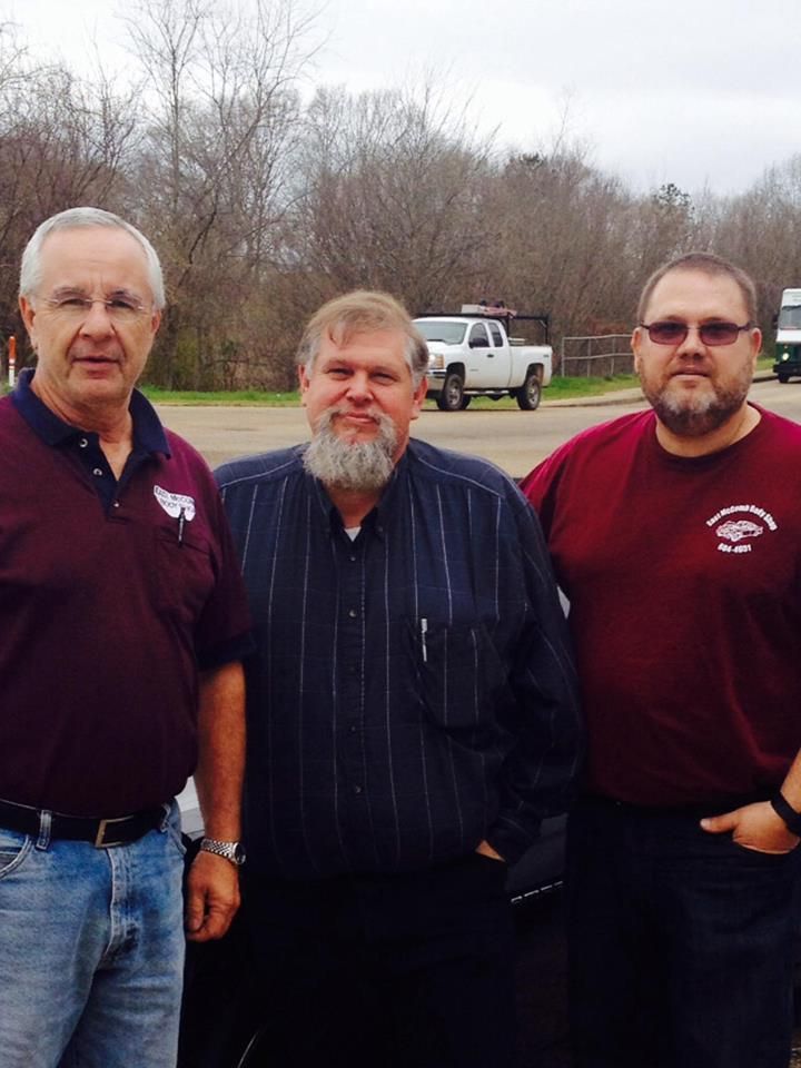 Three men are posing for a picture with a truck in the background