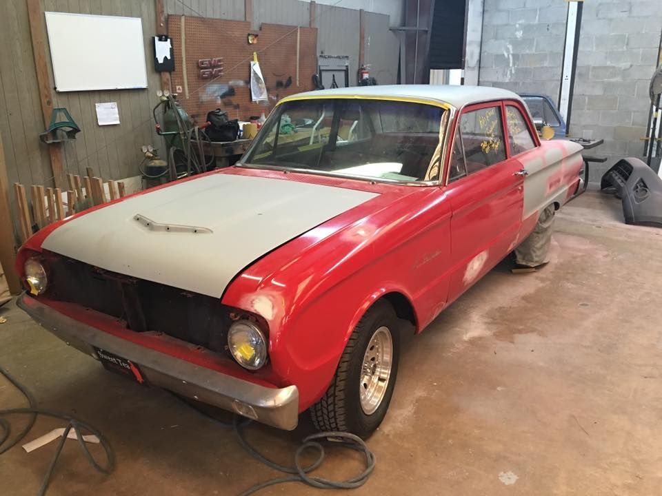 A red car with a white hood is parked in a garage.