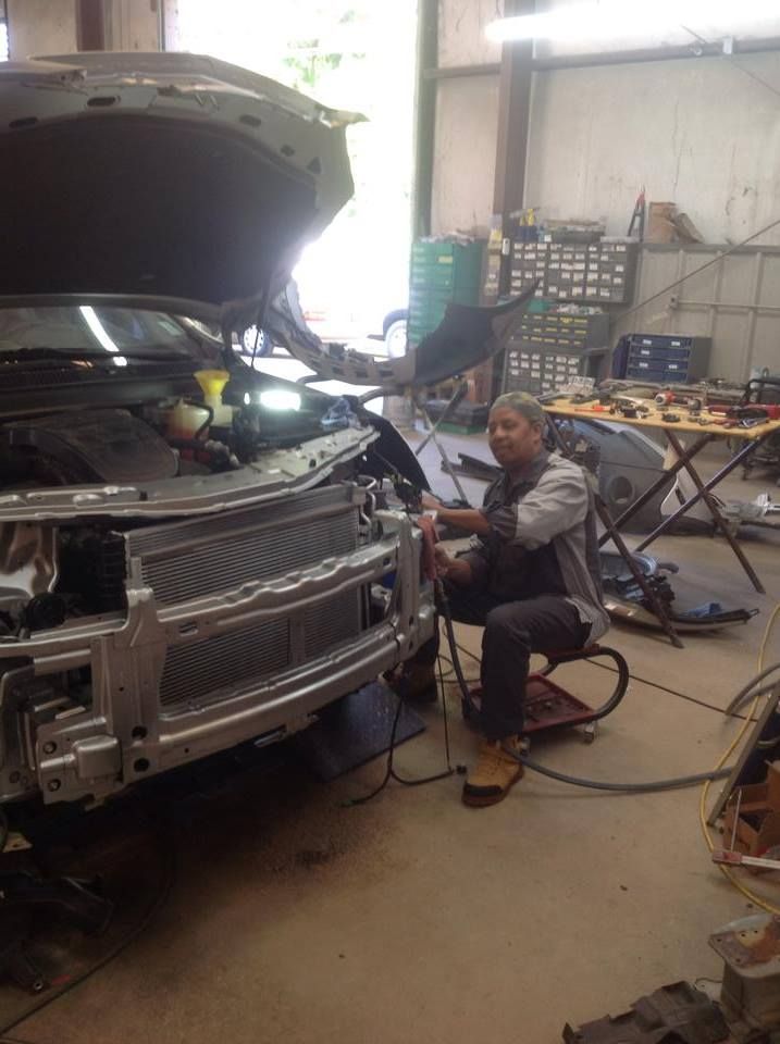 A man is working on a car in a garage with the hood open.