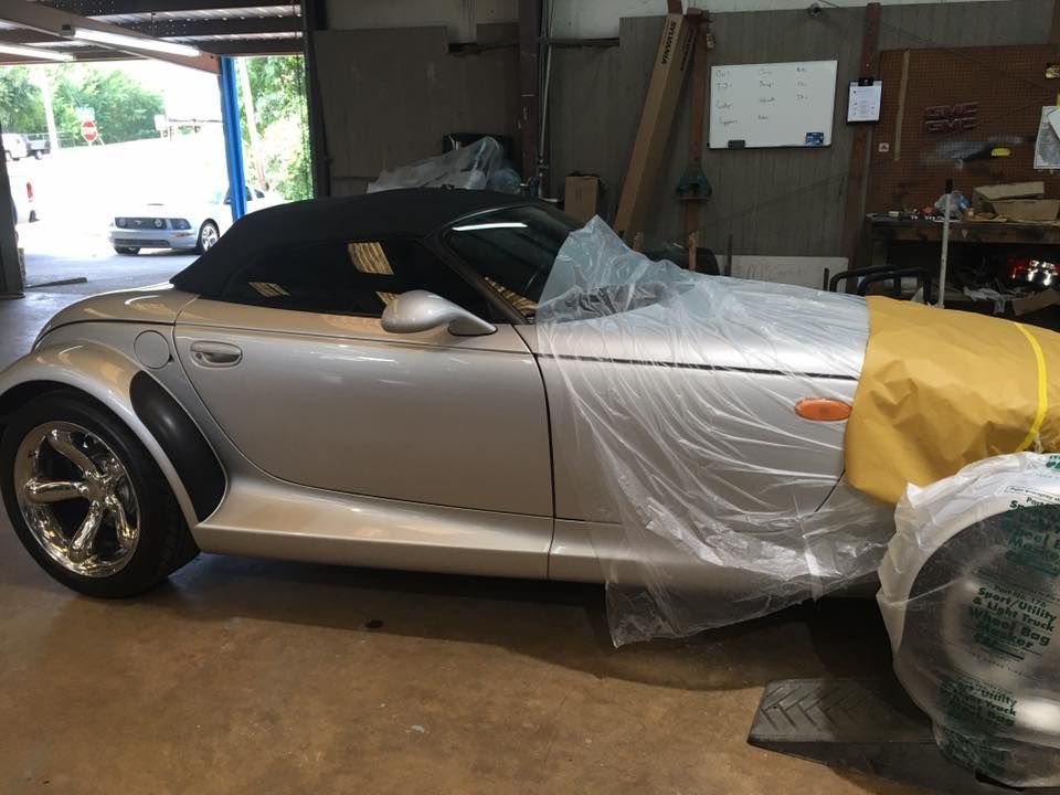 A silver sports car is wrapped in plastic in a garage