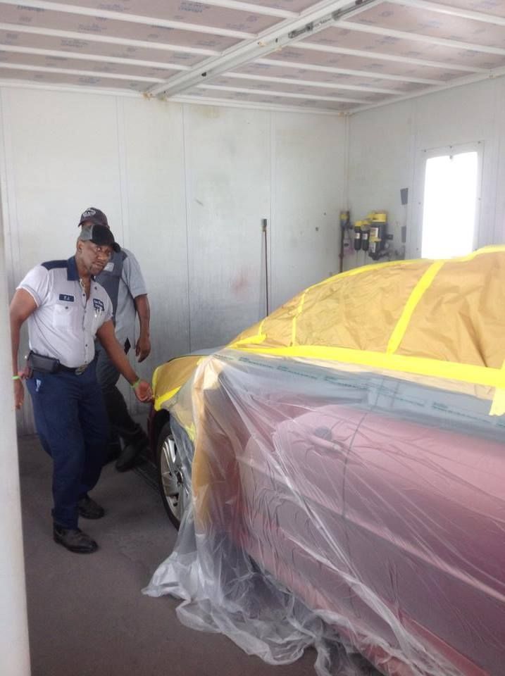Two men are standing next to a red car covered in plastic.