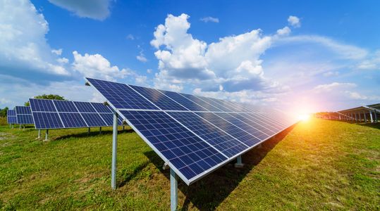 Solar panels in a green field at sunset under a blue sky with clouds