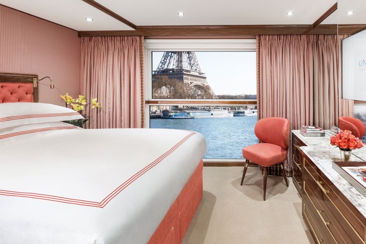 Uniworld Paris Riverboat Cruise. Ultra Luxury Cruising. Bedroom on a ship with a view of the Eiffel Tower through a large window; pink decor.