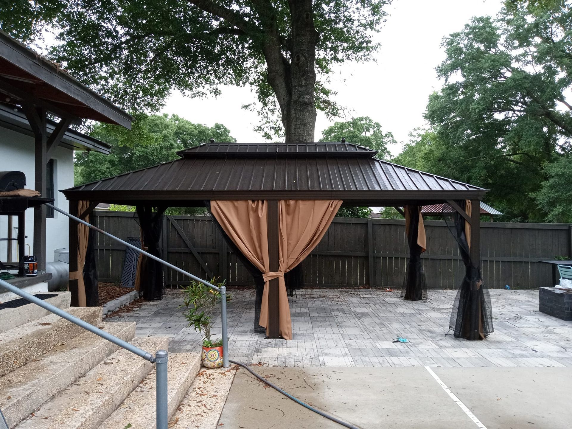 A gazebo with a brown curtain is in the backyard of a house.