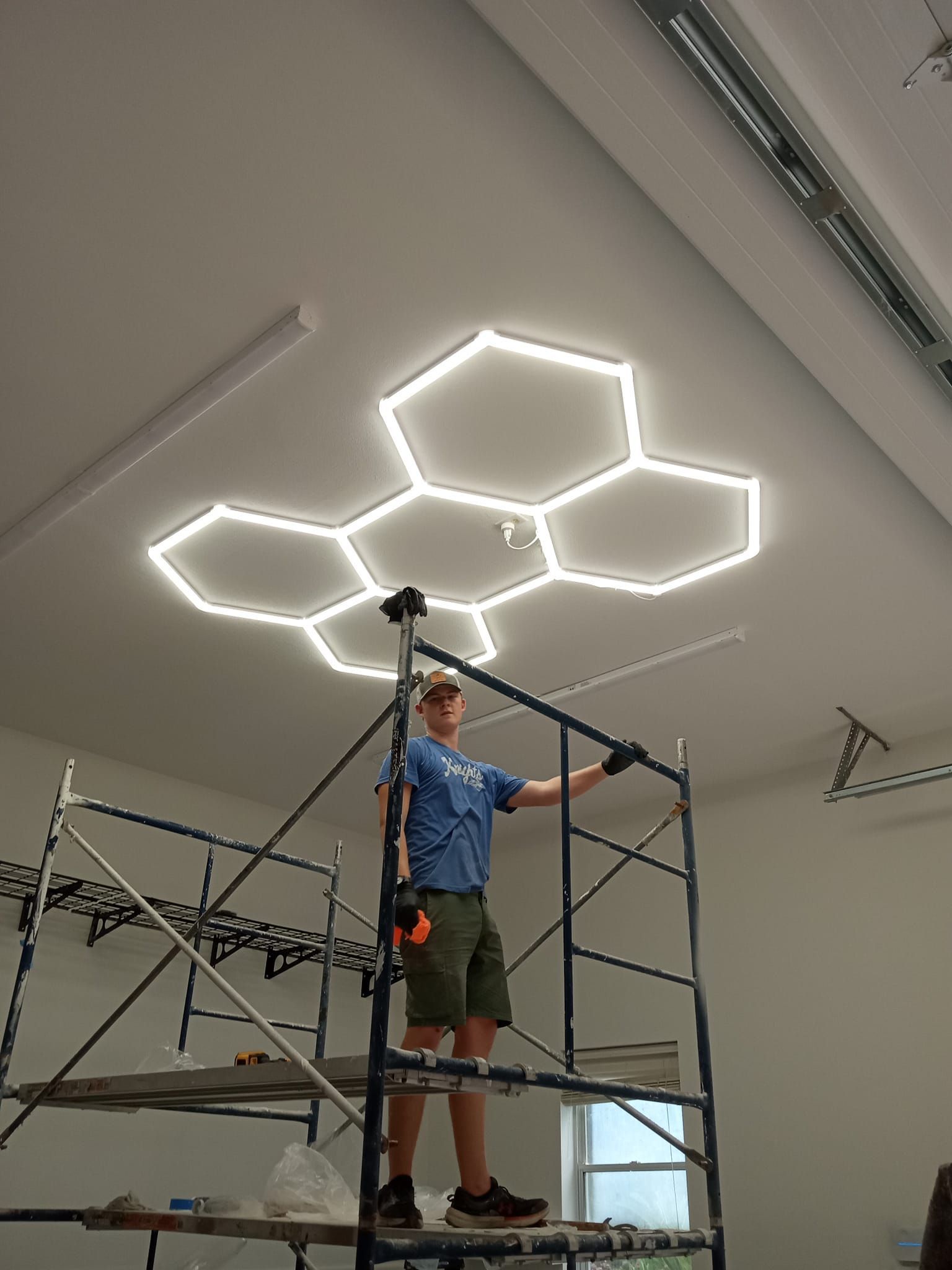 A man is standing on a scaffolding in front of a ceiling with hexagons on it.