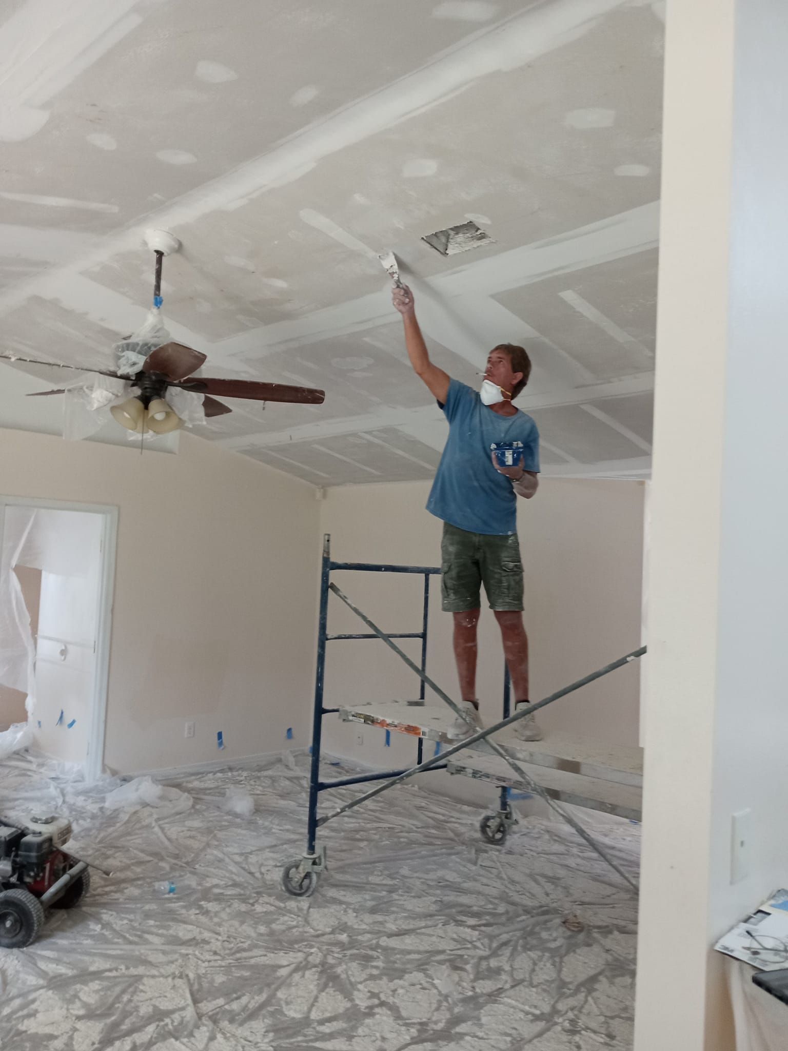 A man is standing on a scaffolding painting the ceiling of a room.