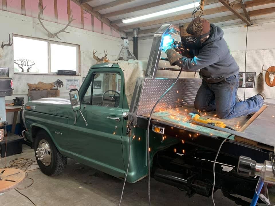 A man is welding a green truck in a garage.