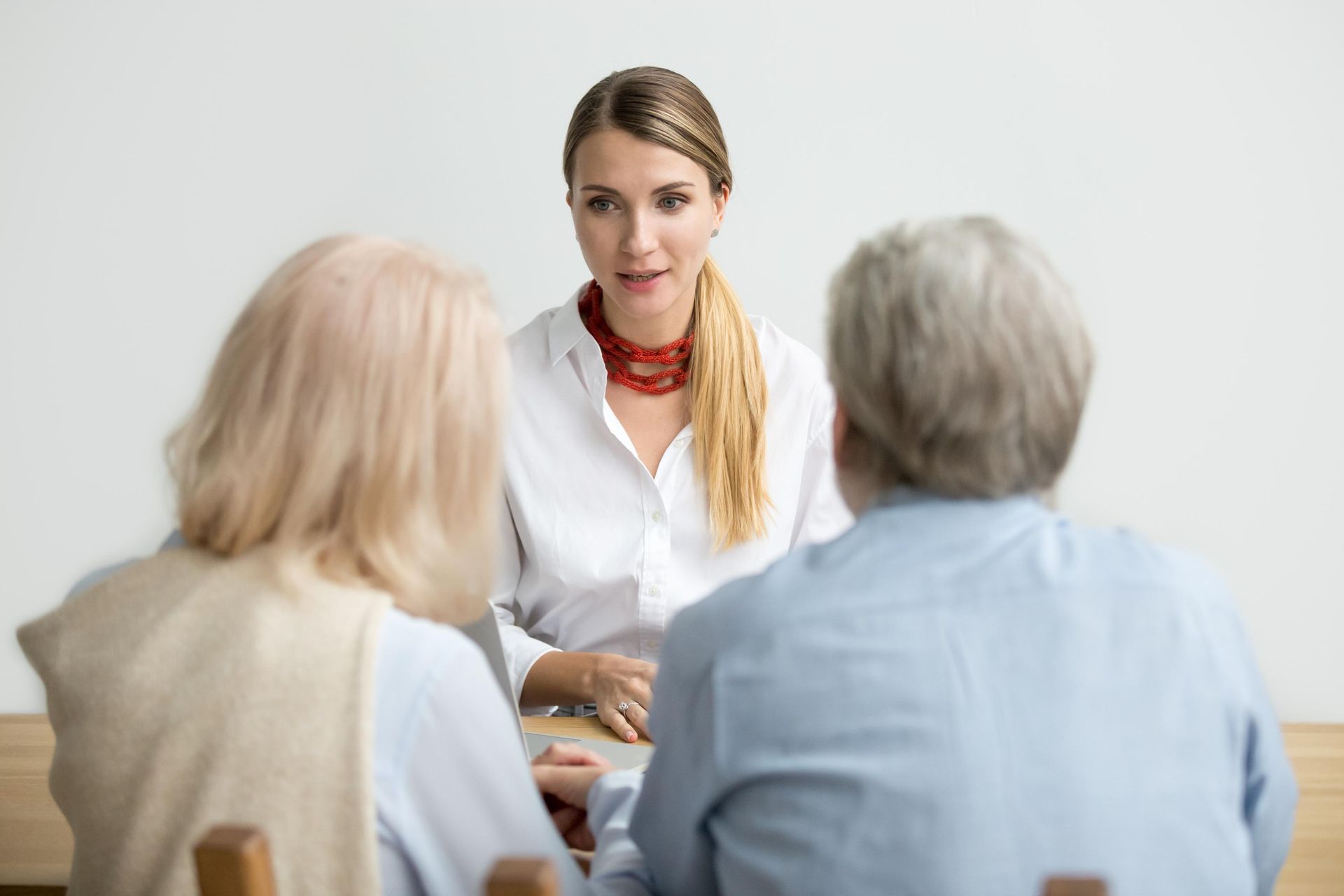Woman in white shirt speaks to a couple seated at a table.