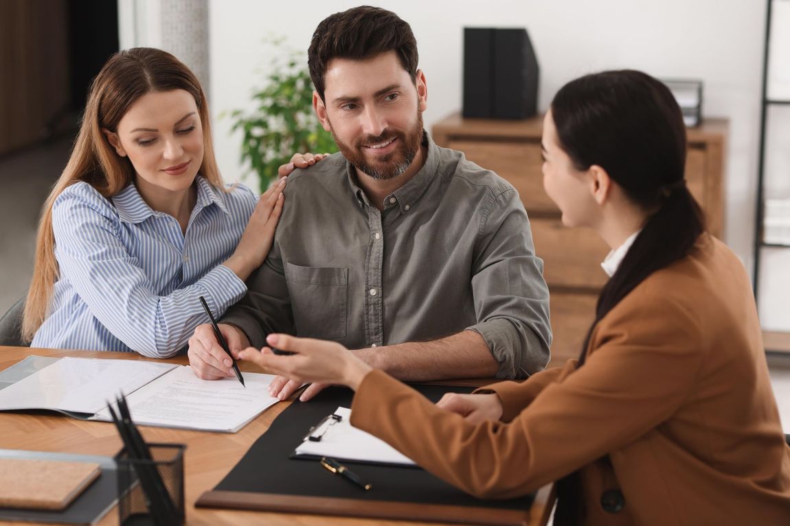 Couple signing documents with a consultant at a desk; a woman points.