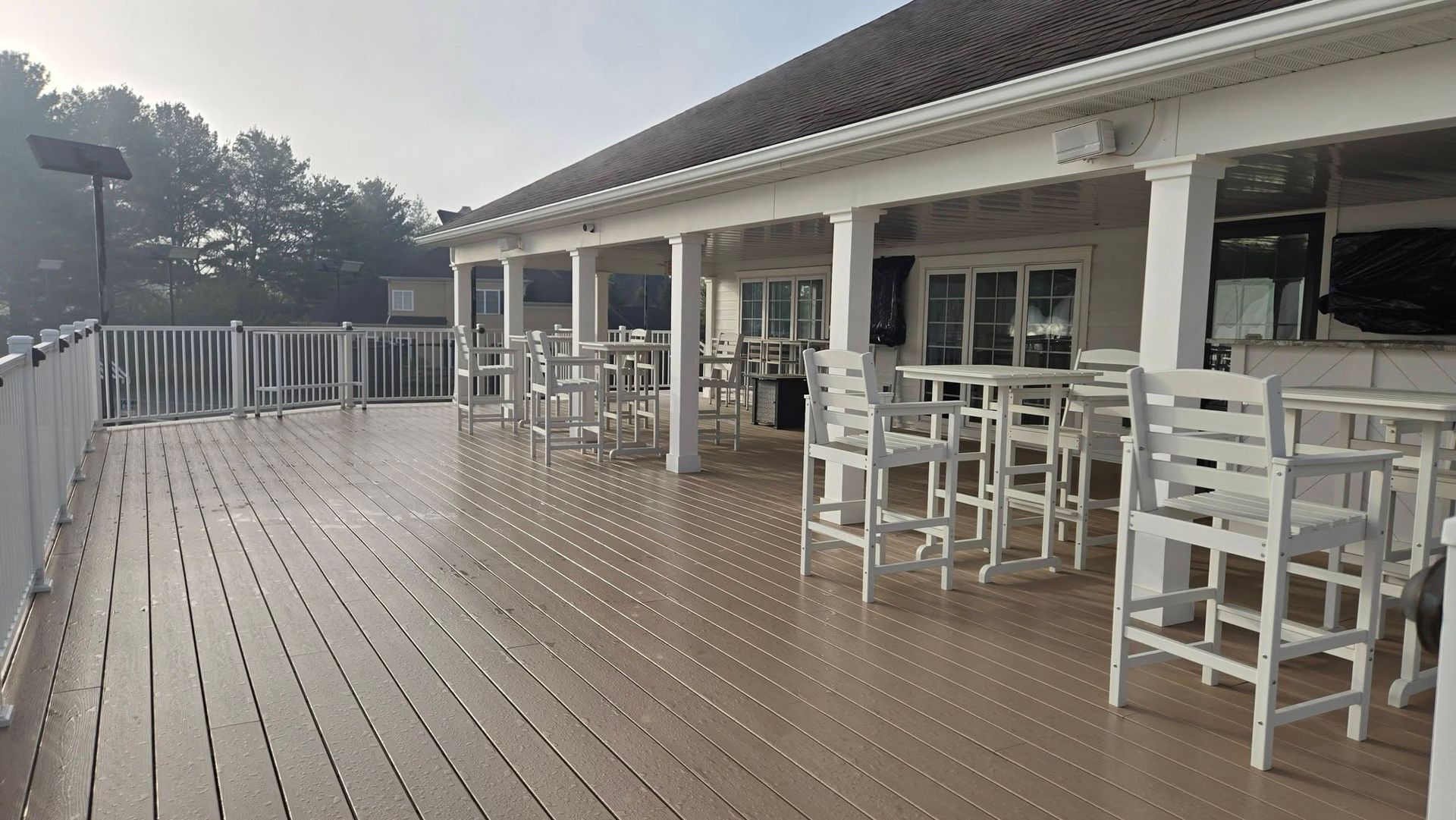 Rain-soaked wooden deck with white patio tables and chairs outside a covered building