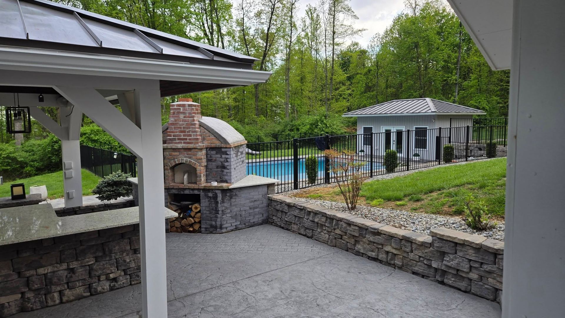 Backyard patio with stone fireplace, pool, and white gazebo surrounded by trees and landscaping