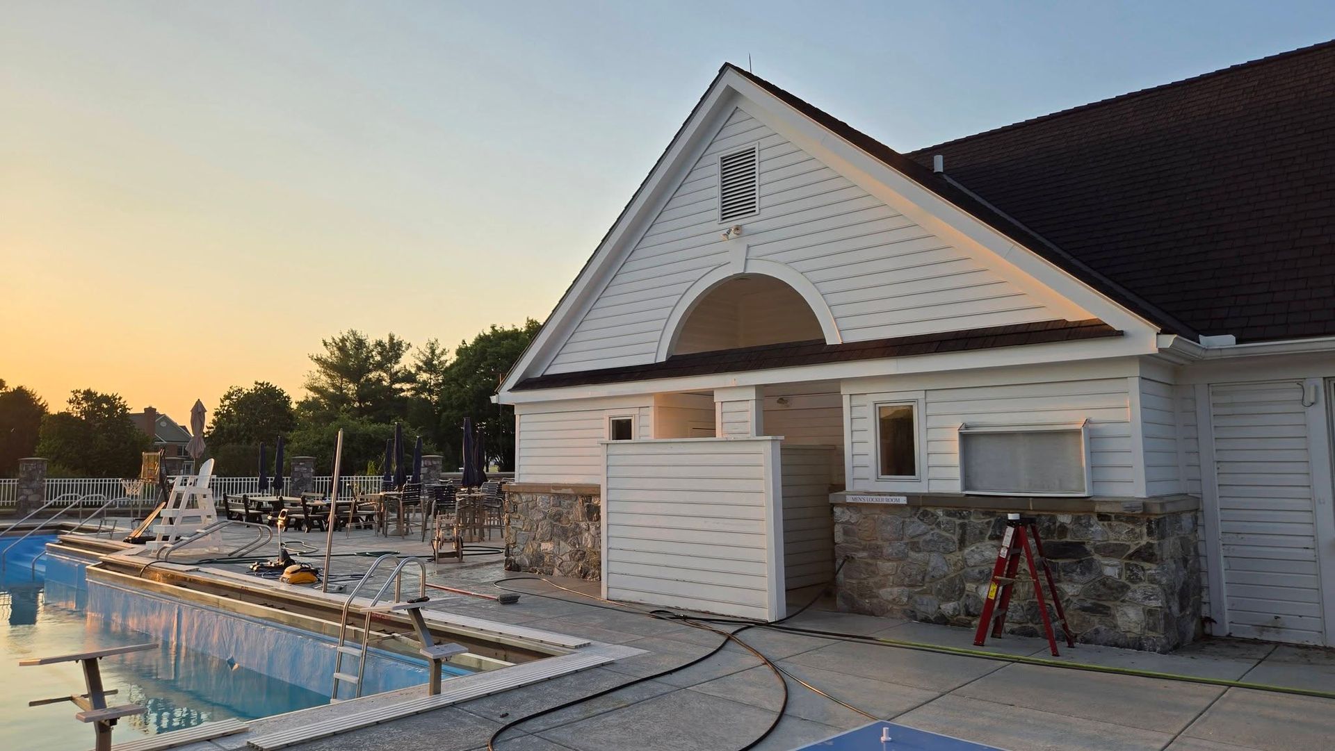 Poolside building under construction at sunset, with white siding, scaffolding, and a swimming pool in front