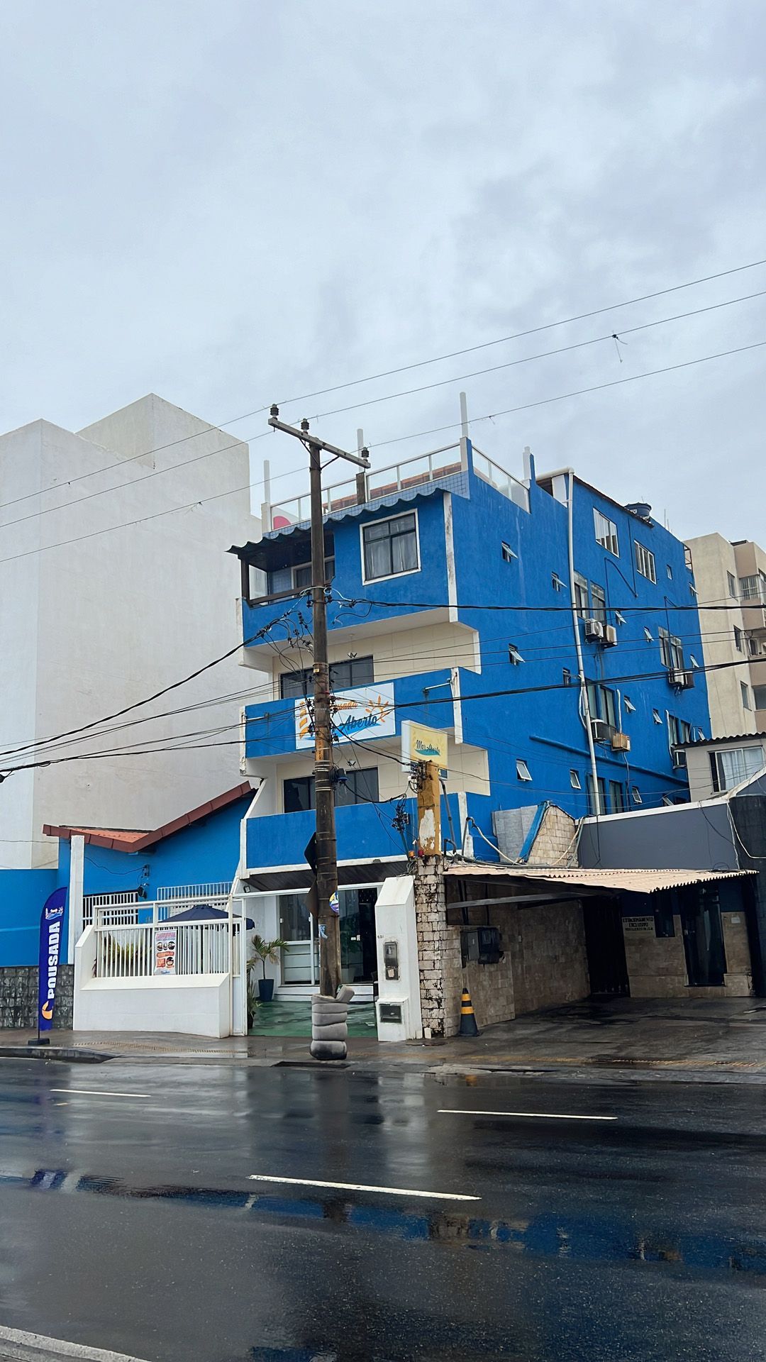 Prédio azul de vários andares em uma rua molhada sob um céu nublado.