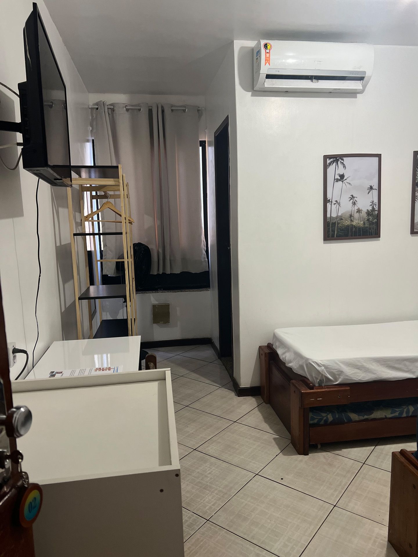 Interior de um pequeno apartamento estúdio com cama, TV, espaço para armazenamento e ar condicionado.
