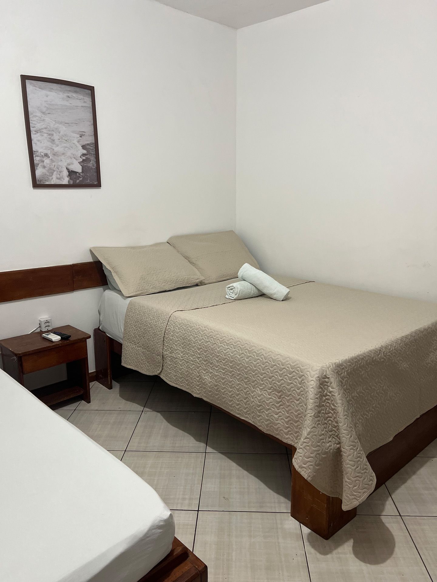 Quarto com duas camas, roupa de cama bege, mesa de cabeceira pequena e obras de arte emolduradas em paredes brancas.