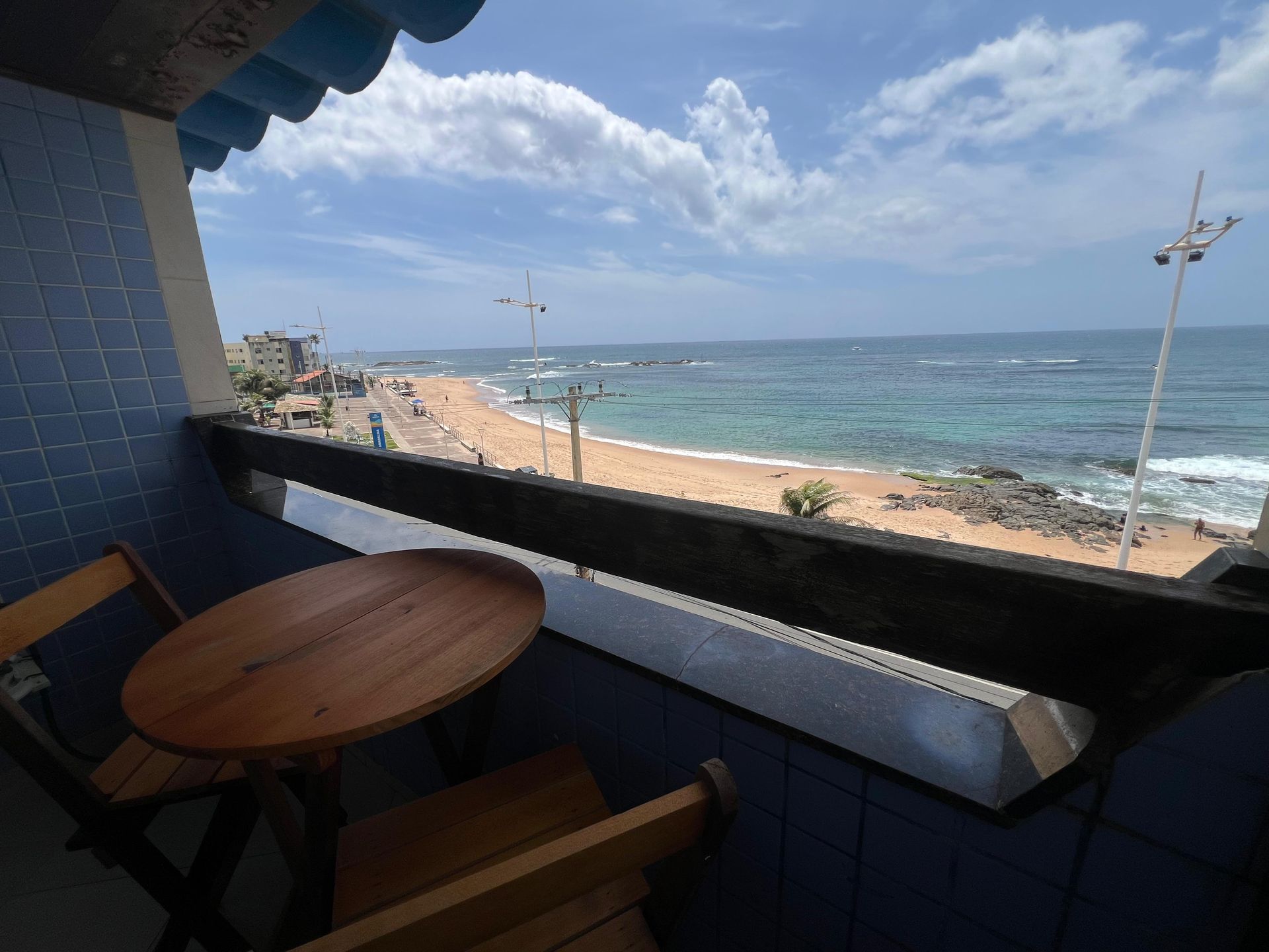 Varanda com mesa e cadeiras com vista para a praia e o oceano em um dia ensolarado.