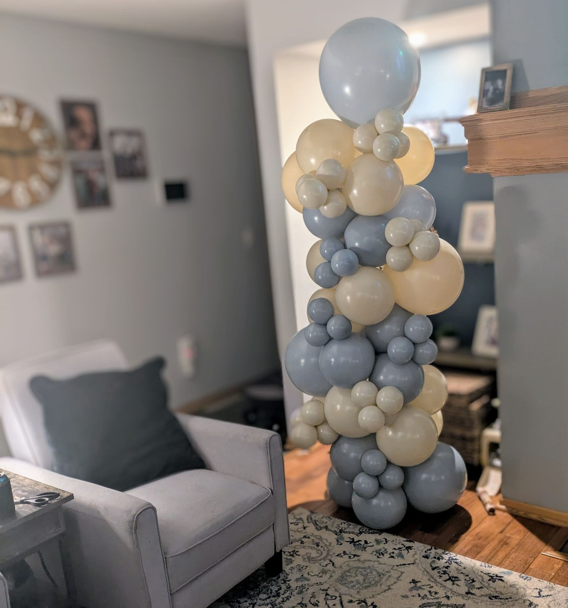 A tall balloon column in shades of blue and yellow stands in a living room next to a white armchair.