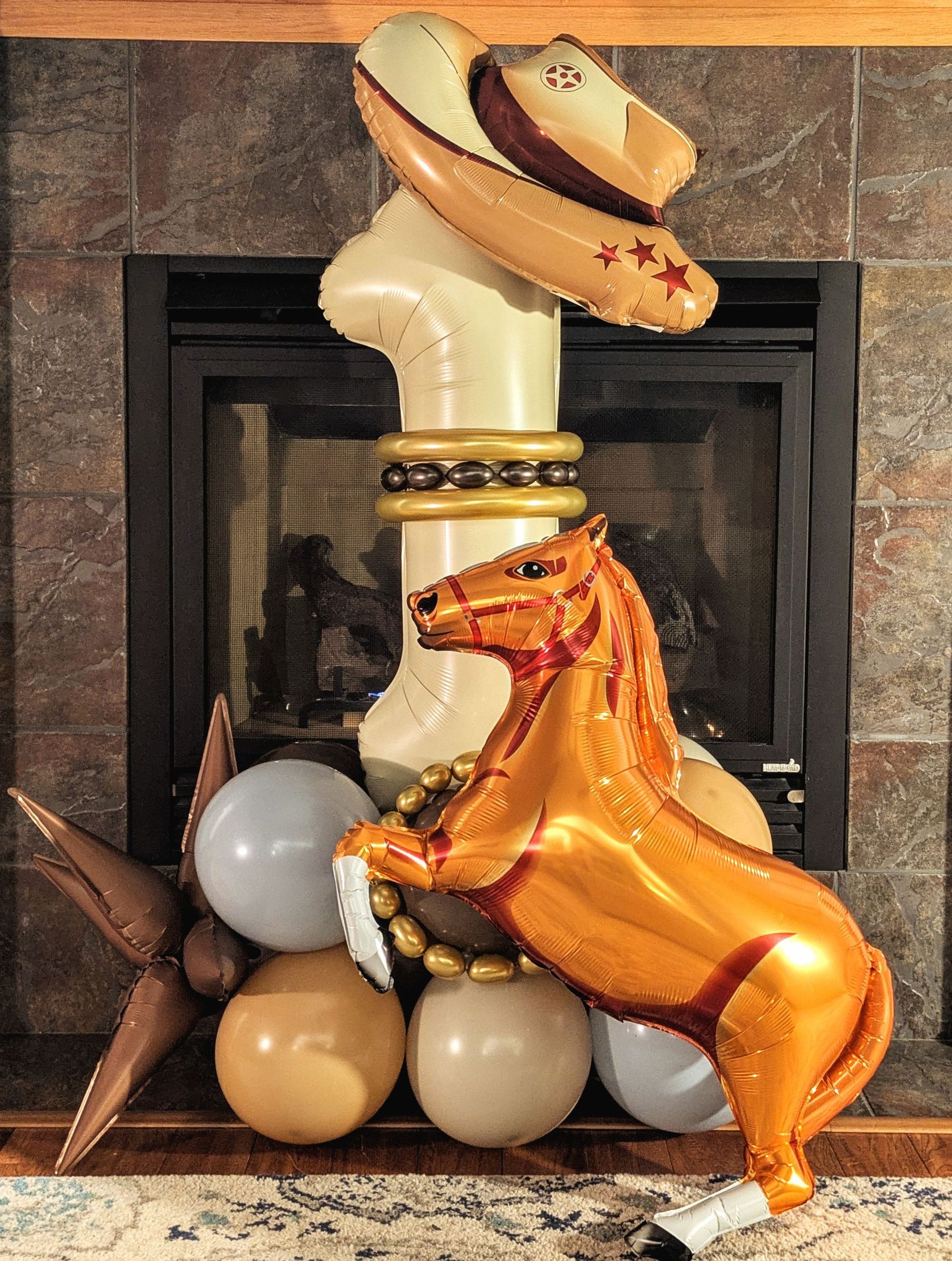 A balloon sculpture of a cowboy-themed display; a horse, cowboy hat, and other balloons are in front of a fireplace.