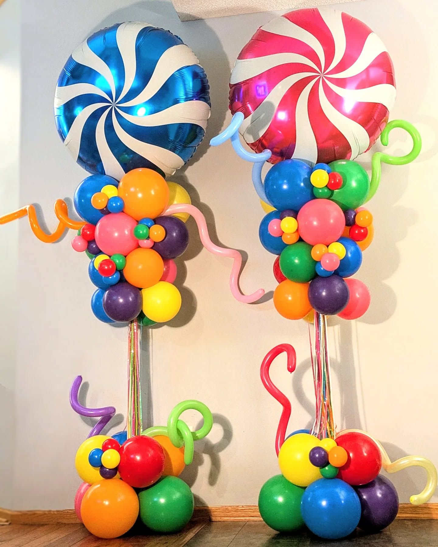 Two balloon sculptures: a blue and a red lollipop-shaped balloon atop colorful balloon stacks with curly accents.