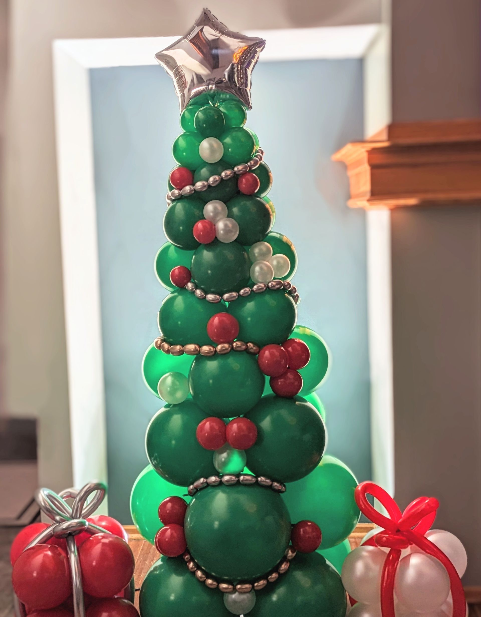 A Christmas tree made of green balloons decorated with red and silver balloons, topped with a star balloon