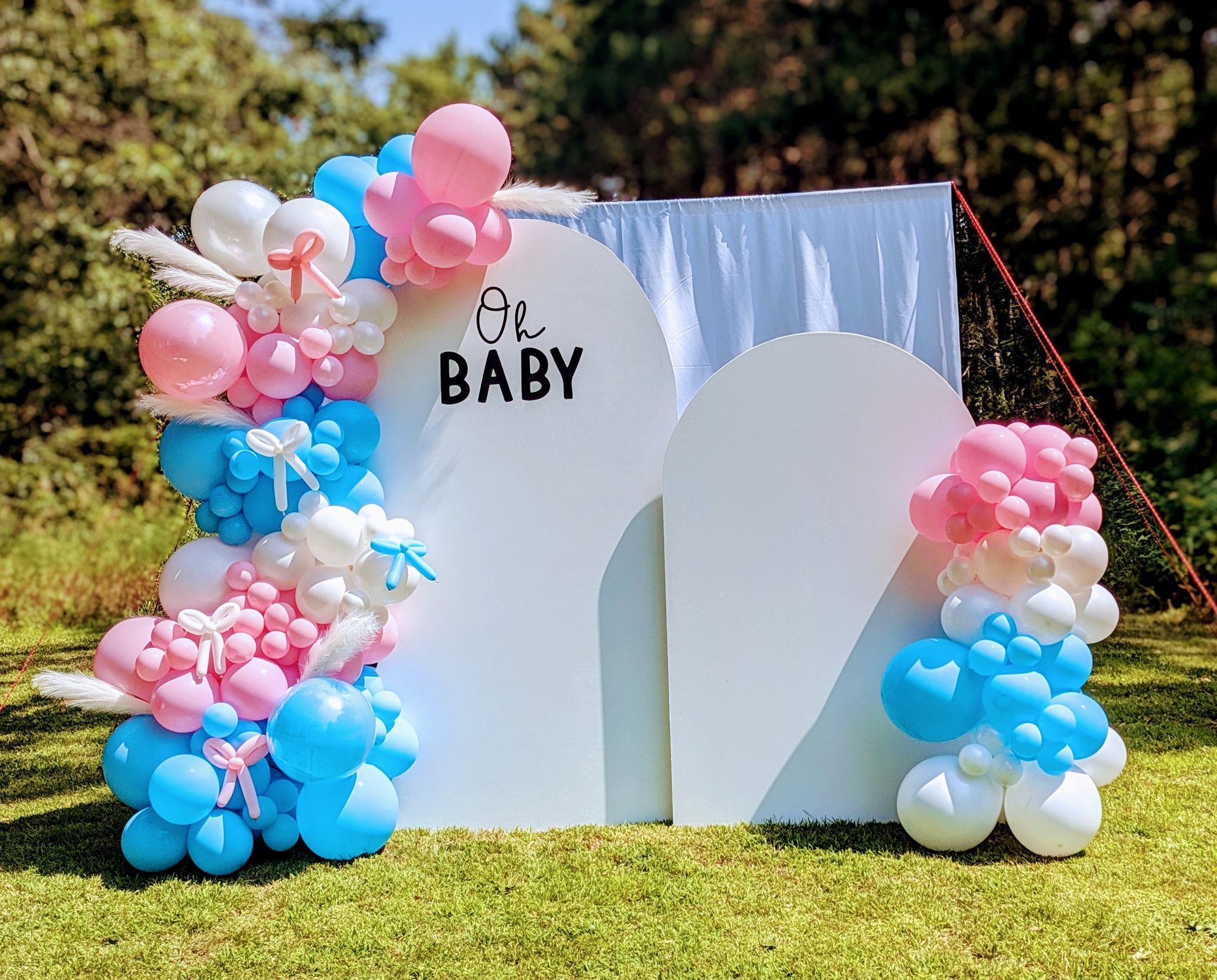 Baby shower backdrop with white arches, balloons in blue, pink, and white, and the words 